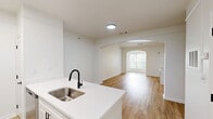 Located at 7000 Johnson Farm Lane in Chadds Ford, PA, this thoughtfully designed one-bedroom, two-bathroom residence offers a clean, modern aesthetic throughout its well-utilized single-floor layout. The open-concept living area immediately impresses with vaulted ceilings and light hardwood flooring, creating an airy and welcoming atmosphere. A white-mantled fireplace serves as a focal point, complemented by pendant lighting and access to a windowed area that brings in natural light and greenery views.

The kitchen is a standout feature, outfitted with white shaker cabinetry, white quartz countertops, a peninsula with a stainless steel undermount sink, matte black fixtures, and stainless steel appliances including an electric range and refrigerator. The layout allows for seamless flow between the kitchen and living spaces.

The bedroom offers a comfortable footprint, fitted with plush carpeting, a large multi-pane window overlooking lush trees, and a six-panel closet door. Both bathrooms are finished with light hardwood-style flooring, white cabinetry, and clean, modern fixtures. One bathroom features a large vanity mirror, quartz countertop, and matte black hardware. A dedicated closet rounds out the functional layout of this well-appointed Chadds Ford residence.