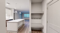 This single-floor residence offers a well-designed layout across two bedrooms and two bathrooms, combining modern finishes with practical functionality. The kitchen serves as a standout feature, equipped with stainless steel Whirlpool appliances, two-tone cabinetry pairing white upper cabinets with warm wood-toned lower cabinets, white quartz countertops, a herringbone tile backsplash, and light wood-look flooring. A kitchen island provides additional counter and prep space.

The living area features wood-look flooring, large windows with horizontal blinds, and a front entry door with a transom window that draws in natural light. Adjacent to the entry is a built-in mudroom nook with a bench seat, upper shelf, and coat hooks—a convenient organizational feature.

Both bedrooms are carpeted and include ceiling fans. The primary bedroom connects to a walk-in closet with multi-tier shelving and hanging rods. The bathrooms feature wood-toned vanities with white quartz countertops, tile-surround soaking tubs, and wood-look flooring. A dedicated laundry room houses a full-size front-loading Whirlpool washer and dryer with overhead shelving. Neutral gray walls and consistent finishes create a cohesive, contemporary ambiance throughout.