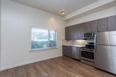 Located at 99 E Sego Lily Dr in Sandy, Utah, this efficiently designed single-floor unit makes smart use of its compact footprint. The layout is anchored by a central hallway that connects the various areas of the space, finished with warm hardwood-style flooring that runs consistently throughout and contributes to a cohesive, inviting atmosphere.

The kitchen is a standout feature, outfitted with a full suite of stainless steel appliances including a gas range, over-the-range microwave, refrigerator, and dishwasher. Rich, dark wood cabinetry provides generous storage, while a clean light-colored countertop and tile backsplash add a polished, modern touch.

The main living area is open and versatile, bathed in natural light from a large window fitted with horizontal blinds that overlooks greenery outside. The elevated ceiling height adds a sense of openness that extends the feel of the room beyond its physical dimensions. Neutral white walls throughout create a clean, bright backdrop adaptable to a variety of uses.

The hallway connects to additional rooms and closet spaces, with flush-mount ceiling lighting providing consistent illumination. An electrical panel is conveniently recessed into the wall. The overall design is clean and contemporary, emphasizing functionality and ease of living within a well-organized, efficiently planned space.