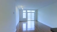 This single-floor space offers a clean, modern aesthetic defined by an open layout and an abundance of natural light. The main living area is anchored by polished hardwood floors that reflect light beautifully throughout the room, enhancing the sense of openness and warmth.

Large windows along the exterior wall allow natural light to pour in, while a full-height glass door provides direct access to an outdoor balcony, seamlessly connecting the interior to the outside. Transom windows above the door further amplify the brightness of the space. The outdoor balcony, visible through the glass, adds an appealing extension to the living area and offers views of the surrounding greenery.

The walls are finished in a crisp white, contributing to the space's fresh and minimalist character. White baseboards provide clean definition along the floors. Track lighting on the ceiling adds a contemporary touch and offers flexible, directed illumination to complement the natural light.

Overall, the space presents a bright, well-maintained interior with modern finishes, thoughtful design details, and a welcoming ambiance suited to a variety of uses and configurations.