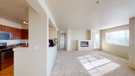 This single-floor residence offers a thoughtfully designed open-concept layout finished in warm, neutral tones throughout. The spacious living area is carpeted and bathed in natural light from multiple windows, creating a bright and welcoming atmosphere. A built-in linear fireplace set into a low partition wall serves as a central architectural focal point, adding both style and warmth to the living space. A door provides direct access to an outdoor area, further enhancing the sense of openness. The kitchen is accessible via a pass-through counter opening, featuring rich wood cabinetry, dark granite-style countertops, stainless steel appliances including a refrigerator, range, and microwave, and light hardwood flooring. Track lighting above the kitchen adds functional illumination. The bathroom includes a wide dual-sink vanity topped with dark stone-style counters, warm wood cabinetry below, and a tub and shower combination. A dedicated laundry room houses a full-sized washer and dryer alongside a water heater. Additional storage is provided by a generously sized walk-in closet fitted with wire shelving. The textured ceilings and consistent neutral palette give the entire space a cohesive, move-in-ready feel.