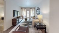 This thoughtfully designed single-floor residence offers a cohesive blend of modern style and comfortable living across its key spaces. The living room serves as the heart of the home, featuring warm wood-look flooring, neutral walls, and generous natural light streaming through large windows and a glass door that opens to the outdoors. A statement oversized roman numeral clock anchors the space, complemented by a plush sofa, layered area rug, and a media console with a wall-mounted television.

The kitchen is outfitted with rich dark cabinetry extending to the ceiling, light countertops, a tile backsplash, and a full suite of stainless steel appliances including a french door refrigerator, electric range, and built-in microwave. Recessed lighting and wood-look flooring complete the functional and stylish space.

The two bedrooms offer soft carpeted flooring and natural light through curtained windows, each providing a calm retreat. Both bathrooms mirror the home's design language, featuring dark vanity cabinetry, light countertops, wood-look flooring, and large mirrors. One bathroom includes a shower-tub combination, while the other offers a streamlined vanity layout. Throughout, the space maintains a consistent, contemporary aesthetic.