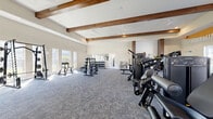 Located at 2950 Landover Blvd in Spring Hill, FL, this expansive single-story fitness center offers a comprehensive workout environment across a generously sized floor plan. The facility is divided into distinct training zones, each thoughtfully designed to support a wide range of fitness activities.

The main strength and cardio area is anchored by soaring ceilings with striking exposed wood beams that lend warmth and architectural character to the space. A bold, eye-catching mural featuring a sunburst design and the motivational phrase "Nothing Works Unless You Do" energizes one wall, setting an inspiring tone throughout. Multiple treadmills and a stair climber are arranged along this mural wall, benefiting from abundant natural light streaming through large windows with outdoor views. The strength training zone features a variety of cable machines, selectorized equipment, free-weight benches, a full dumbbell rack, and a barbell station, all set on durable carpet flooring.

A separate functional training room offers a distinct aesthetic with light hardwood-style flooring, a textured stone-accent wall, tall ceilings, and a large glass garage-style door that fills the space with natural light. This room is equipped with rowing machines, kettlebells, medicine balls, plyo boxes, and TRX-style suspension trainers, making it ideal for dynamic and high-intensity workouts. Together, these areas create a well-rounded, professional-grade fitness facility.
