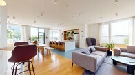 Located at 528 Canal St in Stamford, Connecticut, this thoughtfully designed single-floor space combines a living room and dining area in a clean, contemporary layout. The interior is defined by light-toned herringbone hardwood flooring, crisp white walls, and an abundance of natural light streaming through large floor-to-ceiling windows dressed with sheer linen curtains. The living area features built-in warm wood shelving that houses a mounted television and lush greenery, adding depth and a natural touch to the modern aesthetic. A wall-mounted mini-split system ensures year-round climate comfort. The dining area accommodates multiple wooden tables paired with molded chairs, accented by a curated gallery of framed artwork. A high-top bistro table with bar-height seating offers an additional casual dining option. The space flows seamlessly and is enriched with potted plants throughout, creating a fresh and inviting ambiance. Beyond the interior, the property opens to expansive outdoor amenity areas, including a sparkling swimming pool flanked by lounge chairs and umbrellas, as well as multiple landscaped terraces with lush plantings, seating areas, a pergola, and open sky views — offering a true resort-like experience in the heart of Stamford.