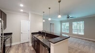 This single-floor residence offers a thoughtfully designed open-concept layout that seamlessly connects the kitchen and living areas. The kitchen is a standout feature, equipped with rich dark cabinetry, striking dark granite countertops, and a full suite of stainless steel appliances including a refrigerator, range, microwave, and dishwasher. A peninsula with pendant lighting above serves as both a functional workspace and a casual dining area, while wood-look flooring grounds the space with warmth and durability. Crown molding adds a refined architectural detail throughout the common areas. The living area extends naturally from the kitchen, finished with plush carpet, a ceiling fan, and windows fitted with blinds that allow for an abundance of natural light and views of surrounding greenery. The bedrooms are carpeted and generously sized, each offering walk-in closets with built-in shelving for ample storage. The bathrooms are finished with matching dark granite vanity tops, tile flooring, and brushed nickel fixtures. One bathroom features a glass-enclosed shower, while another includes a full tub-shower combination with a curved curtain rod. Grab bars are present in the bathrooms, reflecting a thoughtful, accessible design. Overall, the space presents a clean, modern aesthetic with consistent finishes throughout.
