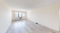 Located at 854-860 E Broadway, Unit 6H in Long Beach, NY, this one-bedroom, one-bathroom residence offers a well-organized layout across a single floor. Light wood-style flooring runs consistently throughout the unit, creating a clean, cohesive aesthetic complemented by warm, neutral wall tones.

The living room is generously sized, featuring large windows that invite natural light and offer views of the surrounding neighborhood. A wall-mounted radiator and built-in AC unit provide year-round climate control. The open feel of the living area makes it highly versatile for various furniture arrangements.

The kitchen has been thoughtfully updated with white shaker-style cabinetry, sleek chrome hardware, and marble-patterned quartz countertops. Stainless steel appliances — including a gas range, microwave, and refrigerator — complete the modern, functional space. Light tile flooring ties the kitchen's clean aesthetic together.

The spacious primary bedroom accommodates a full furniture suite and includes a double-door closet for ample storage. Large windows allow natural light to fill the room.

The bathroom features floor-to-ceiling marble-look tile surrounding a full soaking tub and shower combination, with chrome fixtures adding a polished finish. The overall design of this unit emphasizes clean lines, updated finishes, and a bright, airy atmosphere throughout.