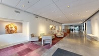 Located at 915 Washington Ave N in Minneapolis's vibrant North Loop neighborhood, this single-floor amenity space offers a generously sized, thoughtfully designed environment spanning multiple distinct functional areas. The main lobby greets visitors with polished concrete floors, colorful patchwork area rugs in warm rose and burgundy tones, and a curated gallery wall showcasing large-format animal photography. Comfortable seating arrangements and a curved reception desk create a welcoming, professional first impression. A secondary entrance also features a concierge-style counter and a dedicated package locker room with natural light from tall, narrow windows. The lounge area is anchored by bold red sofas, a wall-mounted fireplace, and a flat-screen TV, with expansive glass doors opening directly onto an outdoor terrace that brings in abundant natural light and urban views. The fully equipped kitchen features striking red mosaic tile backsplashes, white cabinetry, black countertops, stainless steel appliances including a French door refrigerator, and a central island — ideal for entertaining or communal use. Exposed ductwork and recessed lighting add an industrial-modern edge throughout, while the overall palette of crisp whites, vibrant reds, and warm neutrals creates a cohesive, energetic atmosphere.