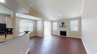 This single-floor residence offers a thoughtfully designed open-concept layout that balances comfort and functionality. The living area is a standout, featuring soaring vaulted ceilings that amplify the sense of space, rich dark hardwood flooring, and a classic tiled fireplace with a white mantle as a focal point. Multiple windows and a sliding glass door flood the room with natural light and provide access to the outdoors. Crown molding and arched architectural details add refined character throughout.

The kitchen is well-equipped for everyday cooking and entertaining, showcasing white cabinetry, granite countertops, stainless steel appliances, and an eye-catching chevron-patterned tile backsplash. A peninsula with bar seating connects the kitchen to the main living space, creating a seamless flow.

The bedrooms are carpeted for comfort, with crown molding and generous closet space. The primary bedroom benefits from a curved bay window arrangement that lets in ample natural light. Both bathrooms are finished with granite-topped vanities, white subway tile surround tub-shower combinations, and hardwood flooring, offering a clean and cohesive aesthetic. The neutral warm-toned palette throughout the home creates a welcoming and versatile ambiance.