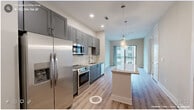 This thoughtfully designed one-bedroom, one-bathroom unit offers a efficient and modern layout across a single floor. The open-concept kitchen and living area serves as the heart of the space, where light wood-tone flooring, recessed lighting, and a sliding glass door leading to a private balcony create a bright, welcoming atmosphere. The kitchen is well-equipped with grey shaker-style cabinetry, a subway tile backsplash, stainless steel appliances including a French door refrigerator, electric range, and built-in microwave. A granite-topped island with pendant lighting above provides additional prep space and casual seating. The living area flows naturally from the kitchen toward the balcony, offering outdoor views through full-length sliding doors. The bedroom features plush carpeting, a dedicated window with blinds for natural light, and access to a walk-in closet outfitted with wire shelving systems for organized storage. The bathroom includes a frameless glass-enclosed shower with marble-style tile surround and contemporary brushed gold fixtures. Light wood-tone flooring extends through the hallway, tying the space together with a clean, cohesive aesthetic throughout.