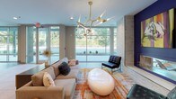 Located at 125 Anderson Hwy in Clemson, SC, this single-floor amenity space combines contemporary design with functional, community-focused areas. The main lounge impresses with floor-to-ceiling windows that flood the room with natural light and offer lush outdoor views, complemented by a striking gold branch chandelier, plush seating, and a vibrant orange-accented area rug. A secondary lounge features a comfortable gray sofa, colorful ottoman seating in orange and blue, and a bold tiger artwork — a nod to Clemson's iconic spirit. The collaborative meeting room stands out with a vivid geometric-patterned accent wall in a multicolor palette, a round white table, modern black chairs, and a statement pendant light. The kitchenette is well-appointed with stainless steel appliances, a built-in sink, stone countertops, and a decorative glass tile backsplash. A coffee and refreshment bar area features a long quartz counter with bar seating, vibrant green open shelving, and a circular pendant light. A dedicated computer workstation nook provides dual monitors for resident use. Polished wood-look flooring, textured tile accent walls, and accessible restroom facilities round out this thoughtfully designed, energetic communal space.