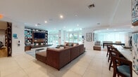 Located at 625 NE Third Ave in Fort Lauderdale, this single-floor community amenity space is designed with a modern, resort-inspired aesthetic that balances function and style. The main lounge area is anchored by a generous sectional sofa, a wave-patterned area rug in aqua and neutral tones, and a built-in media wall with open shelving — all bathed in natural light streaming through floor-to-ceiling glass doors and transom windows that frame views of the outdoor pool area. Large-format tile and warm hardwood flooring transition seamlessly between zones throughout the space. The fully equipped kitchen features granite countertops, stainless steel appliances, mosaic tile backsplash, and a spacious island with bar seating, making it ideal for gatherings and events. Adjacent to the kitchen, a game room offers a pool table alongside additional seating and direct outdoor access. A dedicated co-working and lounge nook is enlivened by a bold, colorful "Bright Life" mural, providing an energetic backdrop for workspace seating. The entry area showcases curated artwork and teal accent walls, establishing a welcoming and contemporary first impression. Throughout, the design integrates vibrant teal accents, rich wood tones, and contemporary art to create a cohesive, upbeat atmosphere.