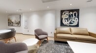 Located at 200 Elgin Street in the heart of Ottawa, this single-floor space offers a thoughtfully designed communal environment that blends functionality with modern sophistication. Light wood-toned flooring runs throughout, creating a warm and cohesive foundation that complements the crisp white walls and recessed lighting overhead.

The kitchen is a standout feature, equipped with stainless steel appliances including a full-size refrigerator and a black range, all set against a striking geometric tile backsplash. Natural wood cabinetry with black hardware lines the walls, while a generous white quartz island with built-in shelving provides ample seating for multiple guests, illuminated by elegant amber pendant lights above.

The two living areas each offer distinct atmospheres. One is a relaxed lounge with tan leather sofas, a patterned area rug, and bold abstract wall art, bathed in warm recessed light. The other is a more open gathering zone featuring swivel armchairs arranged around a round white coffee table, with large windows dressed in sheer roller shades that diffuse natural light generously throughout the room. A formal dining area with a long table, upholstered chairs, and a dramatic dark marble accent wall adds a refined touch. Together, these spaces create a welcoming and versatile environment ideal for both casual gatherings and collaborative use.