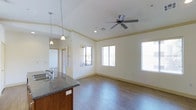 This single-floor residence offers an open-concept layout that connects the kitchen and living areas in a bright, welcoming environment. The living area is generously sized, featuring warm hardwood-style flooring that runs throughout the main space, crisp white walls with crown molding, and multiple windows dressed with horizontal blinds that allow for excellent natural light. A ceiling fan with a sleek modern design is centrally positioned, providing both functionality and a finished look to the room.

The kitchen is thoughtfully designed and flows naturally into the living space, anchored by a kitchen island featuring rich dark granite countertops and warm wood cabinetry beneath. Pendant lighting hangs above the island, adding a stylish focal point and complementing the recessed lighting overhead. The sink is conveniently situated at the island, making the kitchen both practical and social in its orientation.

The overall ambiance of the space is clean, contemporary, and move-in ready, with a neutral color palette that lends itself to a variety of interior styles. The combination of natural light, modern fixtures, and quality finishes creates a comfortable and functional living environment throughout.