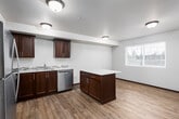 This single-floor residence offers a thoughtfully designed layout with a neutral color palette and consistent dark wood trim throughout. The kitchen serves as a central highlight, featuring rich dark cabinetry, a quartz-topped peninsula ideal for casual dining or prep work, and a full suite of stainless steel appliances including a refrigerator, range, microwave, and dishwasher. Light wood-tone flooring flows throughout the main living areas, complementing the warm cabinetry tones. A secondary kitchenette or utility area is also present, equipped with additional cabinetry, a sink, dishwasher, and a freestanding island with a light countertop.

The living areas connect openly to the kitchen, with windows providing natural light and exterior views. Bedrooms are finished with plush carpeting, neutral walls, and windows that bring in additional daylight. The bathroom is well-appointed with a quartz vanity countertop, a mosaic tile backsplash, and a full tub-shower combination. Notably, a stacked washer and dryer unit is conveniently integrated into the bathroom space, providing in-unit laundry. Overall, the residence presents a clean, modern aesthetic with functional, durable finishes throughout.