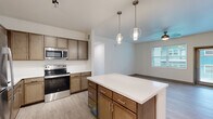 Located at 3234 W 31st St in Pueblo, Colorado, this well-appointed single-story home offers three bedrooms, two bathrooms, and a thoughtfully designed layout that maximizes comfort and functionality. The open-concept kitchen and living area serves as the heart of the home, highlighted by warm wood-toned cabinetry, crisp white countertops, a central island with pendant lighting, and a full suite of stainless steel appliances including a refrigerator, range, and microwave. Light wood-style flooring flows throughout the main living areas, enhancing the bright and airy feel. The adjacent living room features a sleek wall-mounted linear fireplace and a ceiling fan, with natural light streaming in through large windows. The bedrooms are carpeted for warmth and comfort, each equipped with ceiling fans and ample natural light. The primary bedroom includes a generously sized walk-in closet with wire shelving, offering excellent storage capacity. A second walk-in closet with multi-tiered wire shelving provides additional organization options. The bathrooms are finished with wood-toned vanities, white countertops, and a combination tub and shower with brushed nickel fixtures. A dedicated laundry area and four closets throughout complete this practical and modern home.