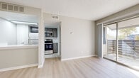 This single-floor unit offers a clean, modern aesthetic with a neutral color palette throughout. The open living area features light wood-style luxury vinyl flooring that extends seamlessly through the main spaces, complemented by a textured ceiling and crisp white baseboards. A sliding glass door floods the living room with natural light and provides direct access to a private balcony, offering a pleasant outdoor retreat.

The kitchen is efficiently designed and outfitted with stainless steel appliances, including a refrigerator, electric range, and over-the-range microwave. Gray cabinetry and a subway tile backsplash add a contemporary touch, while light flooring ties the kitchen visually to the rest of the main living area.

The bedroom is carpeted for comfort and features a window with blinds that allows natural light to filter in. A mirrored sliding closet provides generous storage, and the room connects conveniently to a dedicated bathroom. The bathroom is finished with large-format gray tile surrounding a full soaking tub and shower combination, fitted with chrome fixtures for a polished look.

Throughout the unit, neutral gray walls create a versatile and inviting backdrop, making the space move-in ready and easy to personalize.