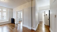 Located at 17 State Street in Troy, New York, Unit 2F is a well-maintained residential space that blends classic architectural character with practical functionality. Rich, dark hardwood flooring extends throughout the main living areas, complemented by tall baseboards and paneled door surrounds that reflect the building's traditional construction. Generous ceiling heights contribute to an open, airy feel across the layout.

The living area is bathed in natural light from a large multi-pane bay-style window, and a classic cast-iron radiator provides warmth during colder months. The open flow between rooms allows for versatile furniture arrangements. Hallways connect the living spaces to private rooms, each featuring the same warm hardwood floors and clean white walls.

The kitchen is equipped with white cabinetry, a stainless steel double-basin sink, gas range, and a refrigerator. A decorative pressed-tin backsplash adds a notable design accent, while light vinyl flooring distinguishes the space from the rest of the unit.

The bathroom features a clean, white vanity with an undermount sink, a framed mirror, and a tub/shower combination. Brushed nickel hardware and wall-mounted lighting complete the space.

Overall, Unit 2F presents a straightforward and functional layout with charming period details, making it a practical option in downtown Troy.