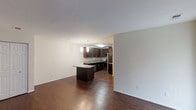 This single-floor space is designed with an open-concept layout that seamlessly connects the living area to the kitchen, creating a spacious and functional environment. Rich, dark hardwood flooring extends throughout, adding warmth and a polished aesthetic to the interior.

The kitchen is a standout feature, showcasing dark espresso-toned cabinetry that reaches toward the ceiling, providing ample storage. A granite or stone-finish countertop runs along the perimeter, complemented by a matching central island that doubles as a breakfast bar or prep space. Pendant lighting above the island adds focused illumination and a contemporary design touch. Stainless steel appliances, including a refrigerator, dishwasher, and microwave, complete the modern kitchen setup.

The adjacent living area is open and airy, framed by clean white walls and smooth ceilings that enhance the sense of space. Recessed lighting supplements the overall brightness of the interior. The neutral color palette throughout creates a versatile backdrop, making the space easy to personalize. The layout promotes an effortless flow between living and cooking areas, ideal for everyday living and entertaining.