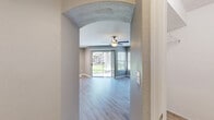 This well-appointed 730-square-foot, single-floor apartment offers 1 bedroom and 1 bathroom, thoughtfully designed to maximize functionality and comfort. The open-concept kitchen and living area serves as the heart of the unit. The kitchen features white shaker-style cabinetry, white quartz countertops, stainless steel appliances including a refrigerator, electric range, and microwave, as well as a center island with an undermount sink. Built-in open shelving adds practical display and storage space. The living room is bright and airy, highlighted by a ceiling fan, a sliding glass door leading to outdoor greenery, and additional windows fitted with horizontal blinds. A built-in shelving niche with an arched accent provides a distinctive architectural detail. The 170-square-foot primary bedroom includes a ceiling fan, a window with natural light, and access to two closets, one of which features wire shelving for organized storage. The bathroom is finished with a white vanity with quartz countertops, brushed nickel hardware, a large mirror, and a full tub/shower combination. Light wood-style flooring runs consistently throughout the unit, complementing the neutral gray wall tones and white trim for a clean, modern aesthetic.