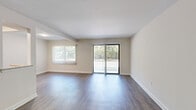 This single-floor, 2-bedroom, 2-bathroom residence offers a clean, modern aesthetic throughout. Wood-look plank flooring runs continuously across the living areas and bedrooms, complementing the crisp white walls and bright, neutral palette.

The living room is generously proportioned, bathed in natural light from a large window and sliding glass door that opens onto a private balcony with leafy outdoor views. Vertical blinds provide flexible light control in this welcoming gathering space.

The galley-style kitchen is thoughtfully designed with dark gray shaker cabinetry, granite-look countertops, a stainless steel sink with a pull-down faucet, and a full suite of stainless steel appliances including a gas range, microwave, refrigerator, and dishwasher.

The primary bedroom is spacious and well-lit, offering ample room for furnishings. Additional built-in closet storage and an in-unit washer are accessible via bifold doors. The second bedroom features a natural light-filled window framed by vertical blinds.

Both bathrooms echo the same refined finishes found throughout, with granite-topped dark vanities. The full bathroom includes large-format tile surrounding a soaking tub and shower combination, while the second bathroom offers a vanity and toilet. A hallway and dedicated closet complete the functional layout.