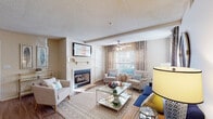The Azalea's two-bedroom, two-bathroom residence in Southaven, Mississippi delivers a thoughtfully designed single-floor layout with a cohesive blend of comfort and functionality. The spacious living room serves as the heart of the home, anchored by a classic fireplace with a white mantle and framed by large windows that allow generous natural light to filter through patterned drape panels. Wood-style flooring and a ceiling fan complete the inviting atmosphere. The galley-style kitchen is efficiently organized with white shaker cabinetry, granite-look countertops, a stainless steel double sink, and black appliances including a refrigerator, electric range, and built-in microwave. Wood-style flooring continues throughout, adding visual continuity. Both bedrooms offer plush carpeting, ample closet space, and windows dressed with fabric curtains, creating a calm and restful environment. Each of the two bathrooms mirrors the kitchen's aesthetic with white vanity cabinetry, granite-look countertops, large mirrors with overhead lighting, and wood-style flooring. One bathroom features a shower/tub combo. The unit presents a consistent, neutral color palette throughout, providing a clean and move-in ready living experience at The Azalea community.
