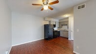 Located at 9805 E 61st St in Raytown, MO, this 2-bedroom, 1-bathroom unit offers a practical and comfortable single-floor layout. Rich, dark hardwood-style flooring flows consistently throughout the space, providing a warm and cohesive aesthetic. The combined kitchen and living area forms the heart of the unit. The kitchen is equipped with gray cabinetry, light granite-style countertops, a full suite of black appliances including a refrigerator, range, microwave, and dishwasher, and a sink tucked neatly into the corner. A textured ceiling carries through the kitchen and into all other rooms. The open living room benefits from a ceiling fan and connects seamlessly to a sliding glass door that leads to a private outdoor patio, allowing natural light to fill the space. Both bedrooms feature neutral gray walls, large windows with blinds for natural light and privacy, and built-in closets with louvered bifold doors. A hallway connects the bedrooms to the full bathroom, which includes a soaking tub with a white tub surround. The layout is efficient and well-organized, making the most of the available space throughout.