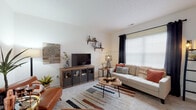 Located at 1 Village Gate Blvd in Delaware, Ohio, this two-floor residence offers a well-organized and comfortable layout across multiple thoughtfully designed spaces. The living room is bright and welcoming, featuring large windows dressed with grommet curtains that invite generous natural light, plush carpeting, and a textured ceiling. The open feel of the room is complemented by wall-mounted shelving, making it both functional and visually appealing. Adjacent to the living area, the dining space accommodates a full-sized table and is accented by pendant lighting and clean white walls. The kitchen is equipped with warm-toned wood cabinetry, light countertops, and a full suite of white appliances including a dishwasher, range, and refrigerator. Light wood-style flooring and a window above the sink add to the kitchen's practical yet inviting character. The bedroom is generously proportioned with soft carpeting, a large closet, and a window that provides ample natural light. Both bathrooms feature warm wood vanity cabinetry, solid countertops, and large mirrors. The overall ambiance throughout the residence is clean, neutral, and move-in ready, offering a comfortable living environment in a residential Delaware, Ohio community.