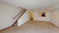 This three-floor residence offers a practical and well-organized layout across its levels. The main living area is generously sized, featuring neutral-toned carpet, recessed lighting, and a pass-through window that connects to the kitchen — ideal for an open, communicative flow between spaces. The kitchen is outfitted with warm wood-toned cabinetry, light stone countertops, and a full suite of black appliances including a range, over-the-range microwave, dishwasher, and refrigerator, all set atop wood-look flooring. A staircase with a warm wood handrail connects the floors, with an upper level that hosts carpeted bedrooms featuring natural light from large windows with vertical blinds and ample closet storage with double wood-paneled doors. The bathrooms are cleanly finished, with one featuring a tiled shower-tub combination, wood-toned cabinetry, and a tall linen tower, while another offers a vanity with a framed mirror and brushed nickel hardware. The lower level includes a dedicated laundry room equipped with a full-size washer and dryer, a utility sink, and wire shelving for additional storage. Throughout the home, neutral wall tones and consistent trim work create a cohesive and functional living environment.