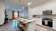 Located at 1400 Henderson Street in Fort Worth, TX, this well-appointed one-bedroom, one-bathroom residence offers a thoughtfully designed open-concept layout. The kitchen is a standout feature, showcasing crisp white shaker cabinetry, a herringbone tile backsplash, quartz countertops, and a full suite of stainless steel appliances including a French door refrigerator, electric range, and over-the-range microwave. A central island with pendant lighting and bar seating connects the kitchen seamlessly to the living and dining areas, making it ideal for both daily living and entertaining. The living room is bright and welcoming, featuring hardwood-style flooring, a ceiling fan, and large windows that invite natural light. The bedroom is carpeted for comfort and includes generous natural light from a large window, with access to a dedicated closet. The bathroom is elegantly finished with a white vanity offering ample drawer storage, quartz countertops, and a glass-enclosed shower. Throughout the residence, dark-trimmed interior doors and high ceilings contribute to a polished, contemporary aesthetic that balances modern style with everyday functionality.