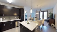 This Art Deco-inspired 2-bedroom, 2-bathroom residence is thoughtfully laid out across a single floor, blending modern design with functional living. The open-concept kitchen is a standout feature, showcasing dark espresso cabinetry, stainless steel appliances including a refrigerator, range, microwave, and dishwasher, and striking quartz countertops with a marble-like finish. A central kitchen island with pendant lighting doubles as a breakfast bar, seamlessly connecting to the dining and living areas. The living room is bright and welcoming, featuring a ceiling fan, a large french door that opens to a private balcony, and views of the outdoors. Both bedrooms are comfortably sized, each equipped with ceiling fans and windows that bring in ample natural light. The primary bathroom features dark cabinetry with sleek hardware, a glass-enclosed walk-in shower, and a double-sink vanity with light countertops. A dedicated in-unit laundry room with full-size washer and dryer adds everyday convenience. Throughout the residence, neutral tones, soft carpeting in the bedrooms, and hard-surface flooring in common areas create a cohesive, modern aesthetic that reflects the Art Deco character of the community.