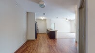 This single-floor unit is designed with an open-concept layout that seamlessly connects the kitchen, dining, and living areas. The kitchen is well-appointed with dark espresso cabinetry, light countertops, black appliances including a refrigerator, microwave, and range, and a peninsula island with a sink that serves as a natural divider between the kitchen and the main living space. Wood-style laminate flooring runs throughout the kitchen and dining areas, adding warmth and visual continuity.

The living area transitions to plush carpeting and features a ceiling fan with a light fixture, along with a sliding glass door that allows natural light to filter in. The bedroom is generously sized, finished with soft carpet, dual windows fitted with blinds for light control, a ceiling fan, and access to a walk-in closet. Neutral walls throughout maintain a clean, versatile aesthetic.

The bathrooms are equipped with dark wood vanity cabinetry, light countertops, large mirrors, and a tub/shower combination. One bathroom also includes open wall shelving, adding a functional design element. Overall, the unit offers a cohesive, practical layout with consistent finishes throughout.