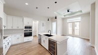 Located at 900 New Day Avenue in Montgomery, TX, this thoughtfully designed 2-bedroom, 2-bathroom home offers a clean, modern aesthetic across a single floor. The open-concept kitchen serves as the heart of the space, showcasing crisp white shaker cabinetry, a large center island with a matte black undermount sink, quartz countertops, stainless steel appliances including a French door refrigerator and double wall oven, a built-in wine cooler, and stylish pendant lighting. Wood-look tile flooring flows seamlessly throughout, adding warmth while maintaining a cohesive design. A stacked washer and dryer unit is conveniently tucked into a dedicated laundry nook off the kitchen. The living area benefits from natural light through glass French doors, complemented by a tray ceiling with a ceiling fan. Both bedrooms are bright and airy, each featuring large black-framed windows with neighborhood views. The primary bedroom includes an en-suite bathroom with a dual-sink white vanity, matte black fixtures, a frameless glass walk-in shower with marble-style tile surround, and direct access to a walk-in closet. The second bathroom mirrors the same refined style. Two well-proportioned walk-in closets with built-in shelving provide ample storage throughout the home.