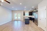 This two-story home in Charlotte, NC offers 3 bedrooms and 3 bathrooms across two well-appointed floors. The main level features an open-concept layout where the kitchen flows seamlessly into the living area. The kitchen is equipped with dark shaker-style cabinetry, granite countertop surfaces, a central island, stainless steel appliances including a refrigerator with ice maker, range, microwave, and dishwasher, complemented by a tile backsplash. Light hardwood-style flooring runs throughout the main level, and French doors provide natural light and outdoor access. A staircase with warm oak wood treads, a classic newel post, and sleek black iron balusters connects the two floors. The upper level hosts all three bedrooms, including a spacious primary suite with a ceiling fan, plush carpet, and a private en-suite bathroom featuring dark vanity cabinetry, granite countertops, a large mirror, and a glass-enclosed walk-in shower. The additional bedrooms are bright and comfortable, each with carpet flooring, ceiling fans, and windows overlooking the surrounding greenery. The home also includes a laundry room, an attached garage, and ample closet storage throughout.
