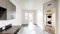 Located at 3050 Mission Inn Ave in Riverside, California, this modern single-floor residence offers a clean, contemporary design throughout. The open-concept living area is finished with light wood-style flooring that extends seamlessly across the main spaces, complemented by crisp white walls and ample natural light streaming in through well-placed windows and a glass door leading to an outdoor balcony area.

The kitchen is thoughtfully appointed with sleek grey cabinetry, dark countertops, and a full suite of stainless steel appliances including a refrigerator, gas range, microwave, and dishwasher. Recessed lighting above the kitchen enhances functionality and adds a polished touch.

A dedicated laundry closet conveniently houses a stacked washer and dryer unit, adding practicality to daily living. The electrical panel is also neatly integrated into the living space wall.

The bedroom features plush carpeting, multiple windows that invite natural light and outdoor views of surrounding greenery, and a clean, spacious layout. The bathroom is finished with wood-style flooring, a dark-topped vanity with an integrated sink, a large mirror, and a grab bar, reflecting both style and accessibility. Overall, the unit presents a bright, move-in-ready living environment in a central Riverside location.