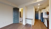 Located in Dallas's vibrant Uptown neighborhood, this single-floor unit at 2801 Live Oak St offers a thoughtfully designed layout with modern finishes throughout. The kitchen is a standout feature, equipped with stainless steel appliances, dark granite countertops, white cabinetry, open shelving, and a striking herringbone metallic tile backsplash with a gold-tone faucet over a stainless undermount sink — a refined combination of form and function. A built-in desk nook with a granite surface provides a dedicated workspace just off the main living area. The spacious living room impresses with a tray ceiling, ceiling fan, and large windows alongside a glass-paneled door that floods the room with natural light and frames views of the Dallas skyline. Rich wood-look flooring flows throughout the entire unit, complementing the warm, neutral color palette. The bathroom features distinctive black-and-white patterned encaustic tile flooring, dark granite counters, white cabinetry, and a glass-enclosed shower. A stacked washer and dryer unit is conveniently tucked within the space. Bold slate-blue five-panel interior doors add a contemporary design accent, completing this well-appointed urban residence.