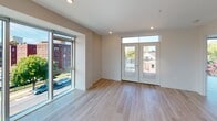 Located at 250 Alexander St in Rochester's vibrant East End neighborhood, this contemporary single-floor residence offers a thoughtfully designed open layout filled with natural light. Light-toned hardwood flooring runs throughout, complementing the clean, modern aesthetic of the space.

The open-concept living and dining area is anchored by dramatic floor-to-ceiling windows that frame sweeping views of the surrounding neighborhood and Rochester skyline. A set of French doors with transom windows provides access to additional outdoor light and city views, while a dedicated bedroom area opens directly onto a private deck, offering elevated views of the urban landscape.

The kitchen is well-appointed with rich walnut-toned cabinetry, a full suite of stainless steel appliances including a gas range, microwave, and refrigerator, and a generous white-topped island with pendant lighting overhead — ideal for both casual dining and entertaining.

The bathroom features a spacious walk-in shower equipped with grab bars and a handheld showerhead, reflecting thoughtful, accessible design. Recessed lighting throughout the unit ensures a bright and welcoming atmosphere. The overall design balances modern minimalism with warm finishes, creating a comfortable and stylish living environment in the heart of Rochester.