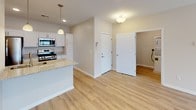 This single-floor unit is designed with a clean, contemporary aesthetic characterized by neutral warm beige walls, light hardwood-style flooring in the main living areas, and plush carpeting in the bedrooms. The open-concept layout connects the living area to the kitchen seamlessly, with ceiling fans installed in both the living room and bedrooms to promote airflow and comfort.

The kitchen is well-appointed with white shaker-style cabinetry, granite-look countertops, and a full suite of stainless steel appliances including a gas range, over-the-range microwave, refrigerator, and dishwasher. A peninsula with pendant lighting above provides additional counter space and serves as a natural transition into the living area.

The living space is generously proportioned, featuring recessed lighting, large windows that invite natural light, and a door providing access to the exterior. The bedrooms are carpeted and comfortably sized, with ceiling fans overhead. One bedroom offers a notable marina view through its window, adding a distinctive outdoor element to the space.

The bathroom features a white shaker vanity with granite-look countertop, a framed mirror, brushed nickel fixtures, and a full tub-shower combination, all set on hardwood-style flooring for a cohesive, polished finish throughout.