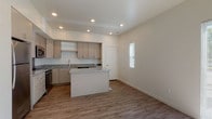 This two-story space presents a clean, contemporary design throughout. The kitchen serves as a central highlight, featuring light-toned cabinetry, granite countertops, and a full suite of stainless steel appliances including a range, microwave, dishwasher, and refrigerator. A substantial kitchen island with matching granite provides additional workspace and anchors the open layout. Recessed lighting illuminates the area, while wood-look flooring adds warmth and continuity across the main level.

The upper level offers multiple carpeted rooms, each benefiting from large windows that invite abundant natural light and outdoor views. One room features vaulted ceilings, adding an airy sense of volume, while another corner room boasts dual oversized windows framing scenic views that include distant mountains. A walk-in closet with built-in shelving and hanging rods provides practical storage.

The bathrooms are consistently finished with granite-topped vanities, light wood cabinetry with chrome hardware, tub-shower combinations, and wood-look flooring. The overall aesthetic is modern and neutral, with a bright, move-in-ready feel throughout both floors.