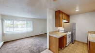 Located at 910 Camino Pescadero in Goleta, CA, this single-story, one-bedroom, one-bathroom residence offers a practical and efficient layout. The galley-style kitchen is well-equipped with warm oak cabinetry lining both walls, tile countertops, a gas range, stainless steel refrigerator, and a sink with ample counter space — all set atop light ceramic tile flooring that continues through the hallway and bathroom areas. The bedroom is a comfortable, well-proportioned retreat featuring plush wall-to-wall carpeting, a textured ceiling, and a window that invites natural light and views of the surrounding greenery. The hallway connecting the main living areas features the same tile flooring and provides access to a closet and the bathroom, which includes a tile-accented vanity with wood cabinetry. The living area, also carpeted, offers a clean, neutral canvas. Baseboard heating is present throughout the unit, ensuring warmth and comfort. The overall aesthetic is clean and straightforward, with white walls and neutral tones creating a bright, livable environment suitable for those seeking a manageable, low-maintenance home in the Goleta area near Santa Barbara.