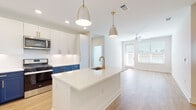 This thoughtfully designed single-floor residence in Brookhaven, Georgia, offers a bright and contemporary living experience with high-quality finishes at every turn. The open-concept kitchen is a standout feature, showcasing a striking two-tone cabinet design with crisp white upper cabinets and bold navy blue lower cabinets, accented by gold hardware. A large center island with a quartz countertop and an undermount sink with a gold-tone faucet serves as the focal point, illuminated by stylish pendant lighting. Stainless steel appliances, including a gas range, microwave, and refrigerator, complete the well-appointed kitchen. In-unit laundry is conveniently accessible just off the kitchen area. Light wood-look flooring flows through the main living spaces, leading to an open living area bathed in natural light from oversized windows and a glass door, with a ceiling fan providing additional comfort. The bedrooms are finished with plush carpeting, ceiling fans, and windows that bring in ample natural light. The bathroom features a clean, modern aesthetic with a glass-enclosed walk-in shower, white tile surround, wood-look flooring, and black matte fixtures. A spacious walk-in closet with built-in shelving provides generous storage. The overall ambiance is fresh, clean, and move-in ready.