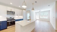 This thoughtfully designed single-floor residence in Brookhaven, Georgia, offers a bright and contemporary living experience with high-quality finishes at every turn. The open-concept kitchen is a standout feature, showcasing a striking two-tone cabinet design with crisp white upper cabinets and bold navy blue lower cabinets, accented by gold hardware. A large center island with a quartz countertop and an undermount sink with a gold-tone faucet serves as the focal point, illuminated by stylish pendant lighting. Stainless steel appliances, including a gas range, microwave, and refrigerator, complete the well-appointed kitchen. In-unit laundry is conveniently accessible just off the kitchen area. Light wood-look flooring flows through the main living spaces, leading to an open living area bathed in natural light from oversized windows and a glass door, with a ceiling fan providing additional comfort. The bedrooms are finished with plush carpeting, ceiling fans, and windows that bring in ample natural light. The bathroom features a clean, modern aesthetic with a glass-enclosed walk-in shower, white tile surround, wood-look flooring, and black matte fixtures. A spacious walk-in closet with built-in shelving provides generous storage. The overall ambiance is fresh, clean, and move-in ready.