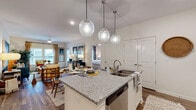 This single-floor residence offers a thoughtfully designed open-concept layout that seamlessly connects the kitchen, dining, and living areas. The kitchen is a standout feature, showcasing white shaker cabinetry, stainless steel appliances, a subway tile backsplash, and a granite-topped island with an integrated sink and built-in dishwasher. Three globe pendant lights hang above the island, adding a contemporary touch. Wood-look flooring flows throughout the main living areas, enhancing the cohesive feel of the space.

The living room benefits from natural light streaming through large windows and provides a comfortable, inviting atmosphere. A dedicated dining area with ample room for a full table sits adjacent to the kitchen.

The space includes two well-sized bedrooms, each with plush carpeting and generous closet space. Both are served by their own bathrooms, each featuring granite-topped vanities with white cabinetry, wood-look flooring, and shower/tub combinations. A dedicated in-unit laundry room accommodates a full-sized washer and dryer with overhead shelving for additional storage. The overall design balances modern finishes with functional living, making this a practical and attractive residence.