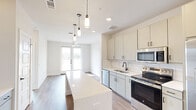 Located at 1735 N Greenville Ave in Richardson, TX, this thoughtfully designed one-bedroom, one-bathroom unit offers a clean, modern aesthetic throughout its efficiently utilized single floor. The open-concept kitchen serves as the centerpiece of the space, showcasing stainless steel appliances — including a refrigerator with ice maker, electric range, built-in microwave, and dishwasher — paired with crisp white cabinetry, a white subway tile backsplash, and a sleek quartz-topped island with pendant lighting above. French doors at the end of the kitchen flood the space with natural light and provide an inviting sense of openness. Wood-look flooring runs consistently throughout, enhancing the home's cohesive, contemporary feel. The bedroom is a calm, bright retreat featuring a ceiling fan, a large window with outdoor views, and neutral walls. A dedicated closet provides practical storage. The bathroom is well-appointed with a tiled tub-shower combo, a vanity with ample counter space and storage, a large mirror with accent lighting, and wood-look flooring that ties back to the rest of the unit. Built-in shelving and a wine rack add functional character to the kitchen area, making this a well-rounded and stylish living space.