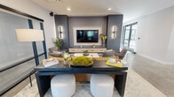 Located at 400 Waterside Dr in Norfolk, Virginia, this thoughtfully designed space offers a seamless blend of modern aesthetics and functional living. The open-concept layout accommodates both a sophisticated lounge area and a fully equipped kitchen, creating a versatile environment ideal for gathering and entertaining.

The lounge area is anchored by a striking shiplap accent wall finished in deep charcoal gray, framing a large wall-mounted flat-screen television with a built-in media console. Sleek vertical sconce lighting flanks the display, casting a warm, ambient glow. Comfortable seating — including a bold mustard leather sofa and accent chairs — surrounds a dark wood coffee table accented with natural greenery, all arranged atop a soft area rug over polished concrete flooring. Glass-panel partitions lend an airy, transparent quality while defining zones within the space.

The kitchen is a standout feature, showcasing quartz countertops with dramatic veining atop a shiplap-clad island and expansive counter runs. Light wood cabinetry paired with matte black hardware and stainless steel appliances — including a gas cooktop and wall oven — exudes contemporary refinement. Elegant globe pendant lights illuminate the island, while a large window allows natural light to pour in. The cohesive design language throughout makes this a polished, inviting space.