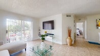 Located at 799 Rich Dr in Deerfield Beach, Florida, this single-story home offers a well-organized layout with a warm, light-filled ambiance throughout. The living room serves as the heart of the space, featuring large sliding glass doors that open to an outdoor patio, flooding the room with natural light. Neutral-toned tile flooring runs throughout, complementing the crisp white walls and textured ceilings found across the home. A wall-mounted flat-screen television and tiered glass coffee table add a modern touch to the living area.

The galley-style kitchen is efficiently designed, featuring warm wood cabinetry, granite-style countertops, stone tile backsplash, and a window that brings in additional natural light. Appliances and ample cabinet storage make the kitchen highly functional.

The home includes multiple bedrooms, each finished with the same tile flooring and textured ceilings. One bedroom features decorative moon-phase mirrors and a bohemian aesthetic, while another offers a bright window with outdoor views. A third bedroom is configured as a children's room with playful décor.

The bathroom includes a wood vanity with granite-style countertops, a large mirror, and a shower-tub combination, maintaining the home's consistent, practical design throughout.