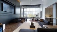 This striking single-floor space exemplifies contemporary design at its finest, combining architectural grandeur with a carefully curated aesthetic. The centerpiece of the space is an expansive floor-to-ceiling glass wall that floods the interior with natural light while framing a breathtaking panoramic view of the surrounding cityscape and greenery beyond.

The open-plan layout is anchored by soaring ceilings, which lend a sense of volume and airiness throughout. Dark hardwood flooring runs seamlessly across the space, providing a warm contrast to the cool, neutral palette of white walls and charcoal-toned structural elements. Industrial-inspired exposed ceiling details add an urban, loft-like character to the overall design.

The living area is thoughtfully arranged with multiple seating zones, each furnished with sleek, low-profile dark sofas and accent chairs. Layered area rugs define individual conversation areas, while gold and brass accent pieces introduce warmth and visual interest. A large wall-mounted media unit anchors one side of the room, balanced by the dramatic transparency of the glass facade on the opposite end.

Sheer floor-to-ceiling drapery softens the glass wall, offering light control while maintaining the sense of openness. The result is a polished, modern environment that seamlessly blends comfort, style, and architectural distinction.