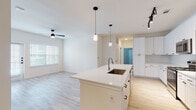 This well-designed single-floor residence offers a bright, open-concept layout that seamlessly connects the kitchen and living areas. The kitchen is a standout feature, showcasing white shaker-style cabinetry, a classic subway tile backsplash, stainless steel appliances including a refrigerator, range, and microwave, and a generously sized center island with a built-in sink and white quartz countertop. Elegant pendant lighting and a track light fixture illuminate the space, while light wood-style flooring flows throughout the main living areas, creating a clean and cohesive aesthetic. The living area is bathed in natural light through large windows fitted with blinds and is equipped with a ceiling fan for added comfort. The bedrooms offer plush wall-to-wall carpeting, neutral tones, and natural light, providing a quiet and comfortable retreat. One bedroom is accompanied by a spacious walk-in closet featuring built-in shelving and a hanging rod for organized storage. Both bathrooms are finished with white cabinetry, white countertops, subway tile surrounds, light wood-style flooring, and brushed nickel hardware — one featuring a tub-shower combination and the other a glass-enclosed walk-in shower. The overall ambiance is clean, contemporary, and move-in ready.