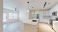 This well-designed single-floor residence offers a bright, open-concept layout that seamlessly connects the kitchen and living areas. The kitchen is a standout feature, showcasing white shaker-style cabinetry, a classic subway tile backsplash, stainless steel appliances including a refrigerator, range, and microwave, and a generously sized center island with a built-in sink and white quartz countertop. Elegant pendant lighting and a track light fixture illuminate the space, while light wood-style flooring flows throughout the main living areas, creating a clean and cohesive aesthetic. The living area is bathed in natural light through large windows fitted with blinds and is equipped with a ceiling fan for added comfort. The bedrooms offer plush wall-to-wall carpeting, neutral tones, and natural light, providing a quiet and comfortable retreat. One bedroom is accompanied by a spacious walk-in closet featuring built-in shelving and a hanging rod for organized storage. Both bathrooms are finished with white cabinetry, white countertops, subway tile surrounds, light wood-style flooring, and brushed nickel hardware — one featuring a tub-shower combination and the other a glass-enclosed walk-in shower. The overall ambiance is clean, contemporary, and move-in ready.