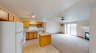 This single-floor residence offers a practical and functional layout with a well-connected open-concept design. The kitchen is equipped with warm honey-toned wood cabinetry, light countertops, tile flooring, a full suite of white appliances including a refrigerator, electric range, and dishwasher, plus a central island that provides additional workspace and storage. Track lighting overhead brightens the kitchen, which flows seamlessly into the expansive living and dining area. The living area features soft wall-to-wall carpeting, a ceiling fan, a fireplace, a wall-mounted air conditioning unit, baseboard heating, and a sliding glass door that opens to an outdoor balcony, filling the space with natural light. A dining area with a pendant light fixture connects the kitchen and living spaces. The bedrooms are carpeted and include baseboard heating and windows with blinds. The bathrooms feature tile flooring and warm wood cabinetry; the primary bathroom includes a dual-sink vanity with a large mirror and a shower area. A dedicated laundry room houses a full-size washer and dryer alongside a water heater, providing convenient in-unit utility. Overall, the space presents a clean, neutral palette with warm wood accents throughout.