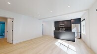 Located at 207 Lucas Ave in Los Angeles' vibrant Echo Park neighborhood, this modern single-story unit offers four bedrooms and three bathrooms with a clean, contemporary design throughout. Light-toned wood flooring runs continuously across the living areas and bedrooms, lending warmth and visual continuity to the space.

The open-concept living area flows directly into a stylish, well-appointed kitchen. The kitchen features dark cabinetry with a matte finish, dark granite countertops, a central island with an undermount sink, and a full suite of stainless steel appliances including a gas range, microwave, and refrigerator. Recessed lighting illuminates the kitchen and living areas efficiently.

The bedrooms maintain the same clean aesthetic with white walls, recessed lighting, and light wood flooring. Several rooms feature wall-mounted mini-split HVAC units for individual climate control, and windows allow natural light to filter through. The primary bedroom offers a comfortable footprint with direct access to adjoining spaces.

The three bathrooms are finished in a crisp, minimalist style with large-format white tile, wall-mounted vanities, black-framed glass shower enclosures, and natural light from windows. The consistent use of black hardware and fixtures throughout the bathrooms ties the modern design language together cohesively across the entire unit.
